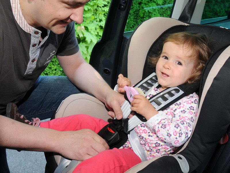 Gefährliche-Kindersitze.jpg Junger Vater schnallt seine Tochter im Kindersitz an.
